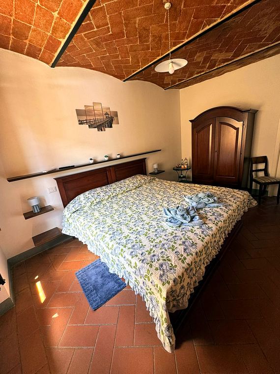 Camera Azzurra: letto matrimoniale con copriletto floreale azzurro e armadio in legno sotto la volta in cotto